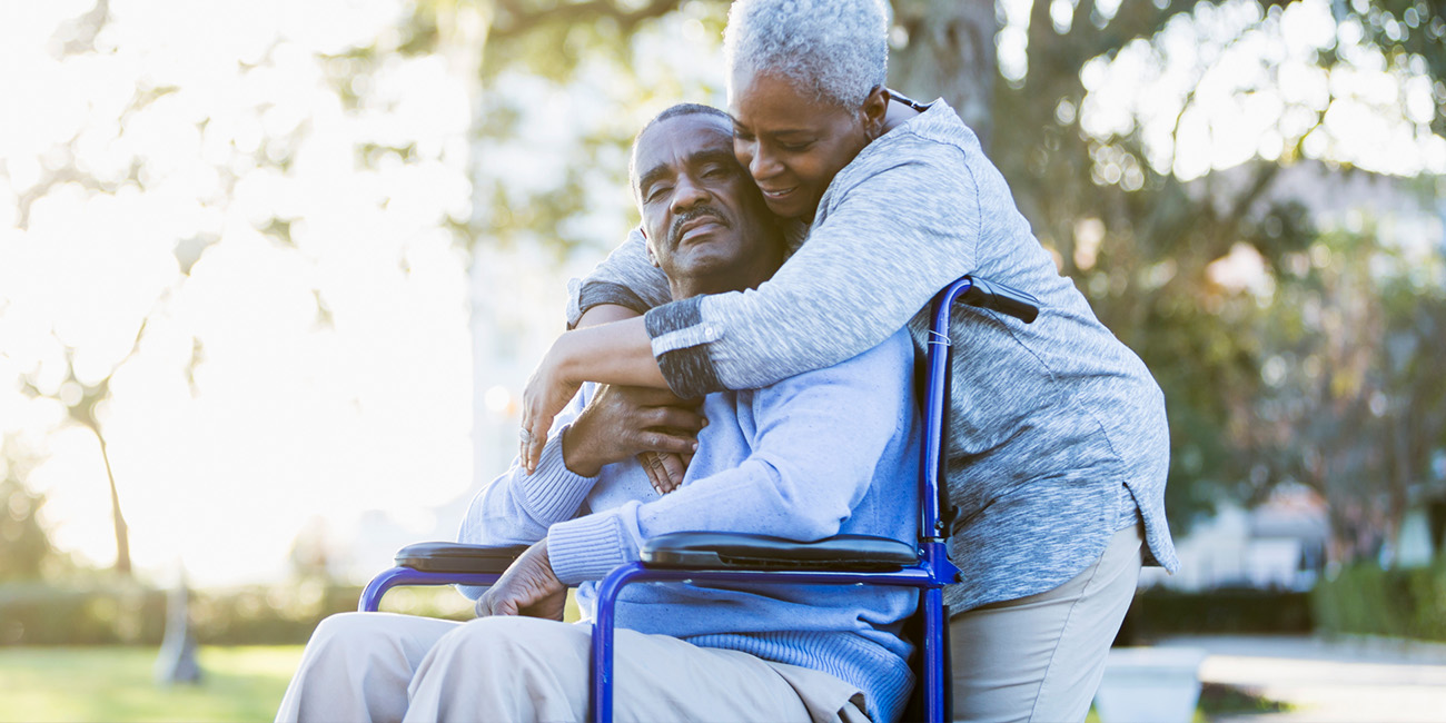 AOT-Oct-CriticalIllness Husband and wife hugging. Husband in a wheelchair