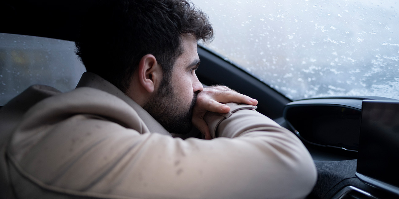 Young man sitting in his car while it snows